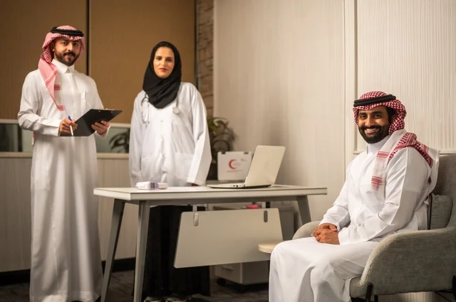 مساعد يقوم بتسجيل حالات المرضى, طبيبة عربية خليجيةة سعودية ترتدي المعطف الأبيض تقوم بشرح الحالة المرضية لمريض يرتدي الشماغ والثوب التقليدي، الحوار مع المرضى لكشف الحالة، تقديم الاستشارات في المراكز الطبيه, العمل في القطاعات الصحية، متابعة السجل الطبي للمراجعين