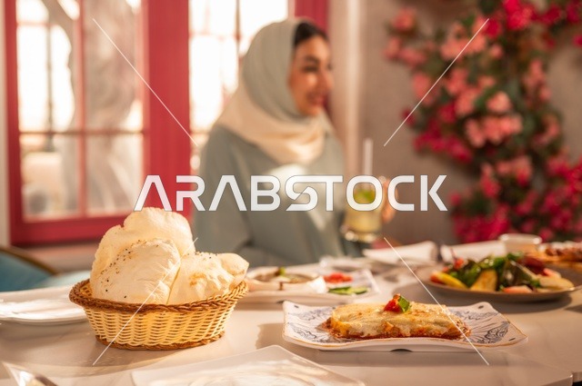 A table filled with a variety of Western foods, having lunch at the restaurant, enjoying recreational activities, a Saudi Arabian Gulf woman wearing a hijab and an abaya sitting at the table, hanging out with friends, gestures of happiness and joy, spending enjoyable times outdoors.