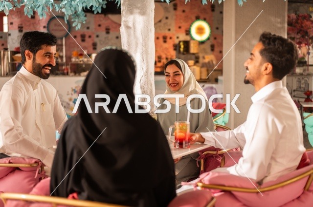 Discussion and dialogue in a calm atmosphere, spending enjoyable times with friends, sharing cold drinks and sweets, building successful social relationships among people, a close-up image of two smiling Saudi Gulf Arab colleagues sitting in one of the upscale cafes with expressions of happiness and joy.