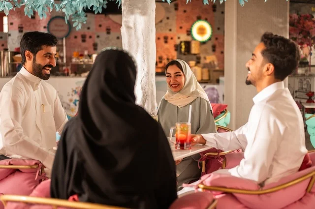 النقاش والحوار في الأجواء الهادئة،قضاء أوقات ممتعة مع الأصدقاء، مشاركة المشروبات الباردة والحلويات، بناء علاقات اجتماعية ناجحة بين الأشخاص، صورة مقربة لزملاء عربيين خليجيين سعوديين مبتسمين يجلسون في إحدى المقاهي الراقية بتعابير السعادة والسرور