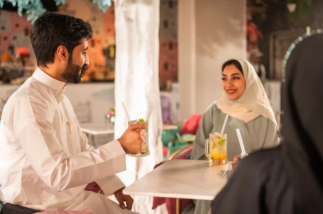 قضاء أوقات ممتعة مع الأصدقاء، النقاش والحوار في الأجواء الهادئة، مشاركة المشروبات الباردة والحلويات والفواكه، بناء علاقات اجتماعية ناجحة بين الأشخاص، صورة مقربة لزملاء عربيين خليجيين اماراتيين مبتسمين يجلسون في إحدى المقاهي الراقية بتعابير السعادة والسرور