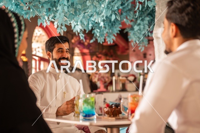 النقاش والحوار في الأجواء الهادئة،قضاء أوقات ممتعة مع الأصدقاء، مشاركة المشروبات الباردة والحلويات، بناء علاقات اجتماعية ناجحة بين الأشخاص، صورة مقربة لزملاء عربيين خليجيين سعوديين مبتسمين يجلسون في إحدى المقاهي الراقية بتعابير السعادة والسرور
