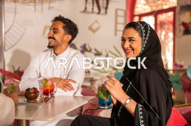 تناول العصائر الموسمية الباردة والمنعشة في المطاعم والكافيهات الفاخرة، جلسة خارجية للترويح عن النفس، تقوية الروابط الزوجية والعائلية، زوجان عربيان خليجيان سعوديان يرتديان الملابس التقليدية السعودية يقضيان أوقات ممتعة برفقة بعضهما البعض