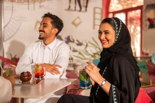 Enjoying cold and refreshing seasonal juices in luxurious restaurants and cafes, an outdoor session for relaxation, strengthening marital and family bonds, a Saudi Arabian couple dressed in traditional Saudi attire spending enjoyable times together.