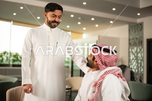 تبادل الخبرات والافكار، دراسة وتحليل المشاريع الجديدة، استخدام جهاز تقني حديث، الوحدة والعمل الجماعي، تطوير العمل وحل المشكلات، رجل عربي خليجي سعودي يرتدي الشماغ والثوب التقليدي يقوم بالعمل برفقة زميله في الخارج، مهنة ووظيفة سعودية مكتبية