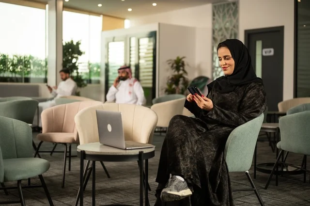 استخدام الهاتف المحمول، عقد الاجتماعات عن بعد, امرأة عربية خليجية سعودية محجبة ترتدي العباءة تعمل على  الحاسوب المحمول في احدى المقاهي الراقية، إنجاز مهام العمل  في الخارج