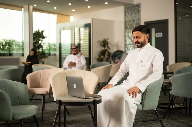 Managing and organizing business affairs through modern technology, completing work tasks remotely, an Arab Gulf Saudi man wearing traditional attire sitting in one of the upscale cafes using a laptop.