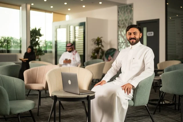 إدارة شؤون الأعمال وتنظيمها عبر جهاز تقني حديث، إنجاز مهام العمل عن بعد، رجل عربي خليجي سعودي يرتدي الثوب التقليدي يجلس  في إحدى المقاهي الراقية ويستخدم الحاسوب المحمول