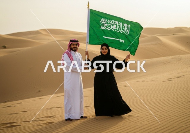 The National Day for the Unification of the Kingdom is September 23. An Arab Gulf Saudi man stands next to his wife holding the Saudi flag, love for the homeland and preserving the identity of the country, the anniversary of the Saudi National Day, Flag Day on March 11, standing in the middle of the desert.