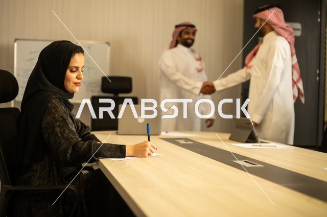 عقد صفقات عمل جديدة ناجحة بين رجال الأعمال، صداقات وتعارف وبناء علاقات اجتماعية، الشراكة في الأعمال والمشاريع، رجلان عربيان خليجيان سعوديان يرتديان الشماغ والثوب التقليدي يقومان بمصافحة بعضهما، توسيع مجالات العمل، إمرأة ترتدي الحجاب والعباءة تدون البيانات على ورقة