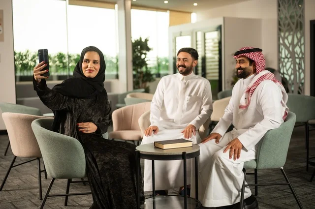 جلسات تعارف وديه, زملاء عمل في اجتماع خارج الشركة, إمرأة عربية خليجية سعودية ترتدي الحجاب والعباءة تقوم باستخدام الجوال برفقة أصدقائها, التقاط صور سيلفي تذكارية عبر الهاتف المحمول, توثيق اللحظات السعيدة