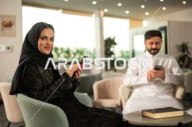 زملاء عمل في اجتماع خارج الشركة, إمرأة عربية خليجية سعودية ترتدي الحجاب والعباءة تقوم باستخدام الجوال برفقة أصدقائها, دمج التكنولوجيا والتقنية بالحياة الروتينية، الجلوس في احدى الكافيهات الراقية، جلسات تعارف وديه