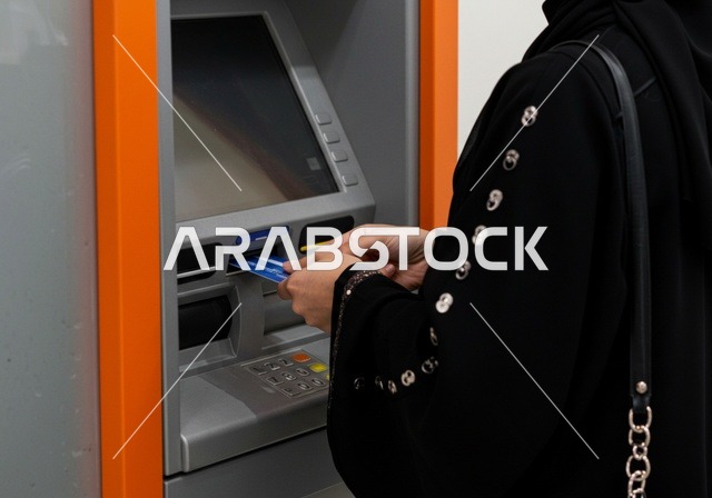 استخدام الوسائل والتقنيات الحديثة،  ، صورة مقربة لإمرأة عربية خليجية سعودية ترتدي العباءة السوداء تقوم بإدخال البطاقة الائتمانية في ماكينة الصراف الآلي، ، سهولة وإمكانية سحب النقود،  الدفع والشراء من خلال البطاقات البنكية