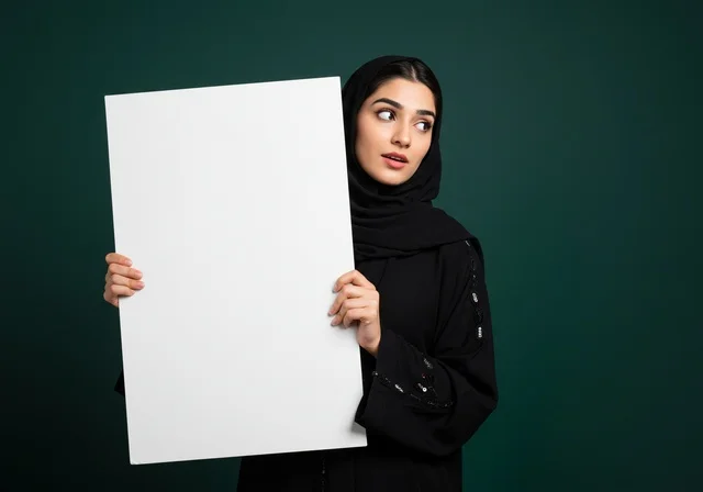 النظر الى الكاميرا بتعابير التخمين, موك اب مربع أبيض, العروض والإعلانات التسويقية, بورتريه مقرب لإمرأة عربية خليجية سعودية محجبة ترتدي العباءة تمسك بيدها لوحة بيضاء مربعة فارغة, لوحات توضيحية ووسائل تعليمية,  خلفية خضراء داكن