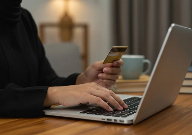 نقل المعلومات من بطاقة صفراء غلى جهاز الحاسب المحمول، صورة مقربة لأيدي إمرأة عربية خليجية سعودية ترتدي عباءة سوداء تحمل بيدها بطاقة بنكية باللون الاصفر، مفهوم الأنوثة والنعومة، المهارة الكتابة السريعة على لوحة المفاتيح