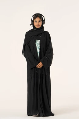 الاستمتاع بسماع الأغاني، التسلية والترفيه بإستخدام تقنية الهيدفون، ارتداء سماعات الرأس الصوتية، بورترية لشابة عربية خليجية اماراتية ترتدي العباءة و الحجاب و سماعات الرأس تقوم بالاستماع للأغاني بايماءات السرور والسعاة، خلفية بيضاء