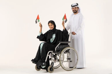 الاعتزاز بالوطن والشعور بالانتماء له، الأعياد والمناسبات الوطنية، بورترية لفتاه عربيه خليجيه عمانية من ذوى الاحتياجات الخاصة ترتدي العباءة و الحجاب تجلس على كرسي متحرك  برفقة زوجها تحمل العلم العماني مع تعبيرات الفخر، خلفية بيضاء
