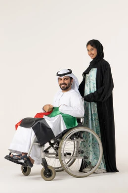 National holidays and occasions, highlighting feelings of patriotism and pride in the country, a portrait of an Arab Gulf Omani man with special needs wearing traditional attire sitting in a wheelchair holding the Omani flag with expressions of pride alongside his wife, gestures of happiness and joy, white background.