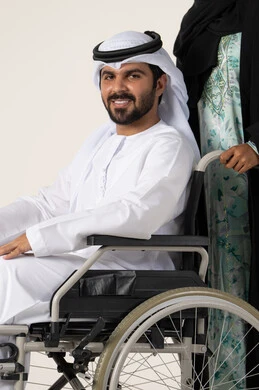 تأمين أدوات ومعدات لمساعدة المرضي، الاخلاص والعطف بين الزوجين، جودة حياة ذوي الهمم في الامارات ، بورترية لرجل عربي خليجي اماراتي يرتدي الكندورة و الغتره مقعد يجلس على كرسي متحرك، امرأة عربية خليجية اماراتية ترتدي العباءة والحجاب تساعد زوجها على التنقل والحركة، خلفية بيضاء