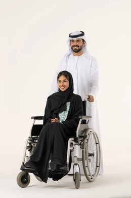 النظر الى شيء ما بتعابير السعادة و السرور، التحسين من نفسية أصحاب الهمم، الإخلاص والعطف بين الأزواج ، مساعدة مرضى ذوي الإعاقة الحركية على التنقل بسهولة, بورترية لامراة عربيه خليجيه اماراتية من ذوى الاحتياجات الخاصة ترتدي العباءة و الحجاب تجلس على كرسي متحرك برفقه زوجها