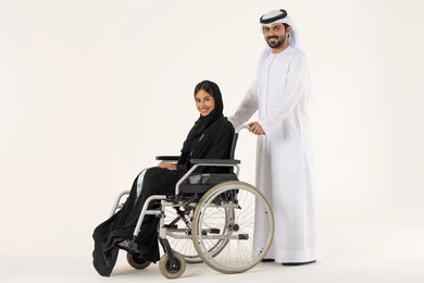 Sincerity and compassion between spouses, improving the mental state of people with determination, looking at the camera with expressions of happiness and joy, helping patients with mobility disabilities to move easily, a side portrait of an Emirati Gulf Arab woman with special needs wearing an abaya and hijab sitting in a wheelchair accompanied by her husband.