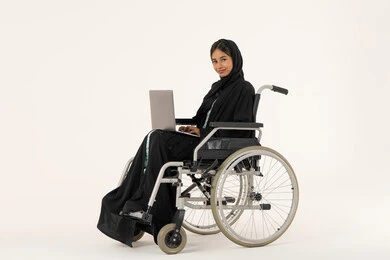 تنظيم العمل وإدارته عن بعد ,انجاز المهام عبرالابتوب , استخدام الأجهزة والتقنيات الحديثة, الاقتصاد والأمور المالية، بورترية من الجانب لامراة عربيه خليجيه اماراتية من ذوى الاحتياجات الخاصة ترتدي العباءة و الحجاب تجلس على كرسي متحرك تعمل على الحاسوب المحمول، خلفية بيضاء
