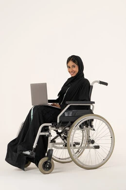 إدارة المشاريع عن بعد ,انجاز المهام عبرالابتوب , استخدام الأجهزة والتقنيات الحديثة, الاقتصاد والأمور المالية، بورترية من الجانب لامراة عربيه خليجيه اماراتية من ذوى الاحتياجات الخاصة ترتدي العباءة و الحجاب تجلس على كرسي متحرك تعمل على الحاسوب المحمول، خلفية بيضاء