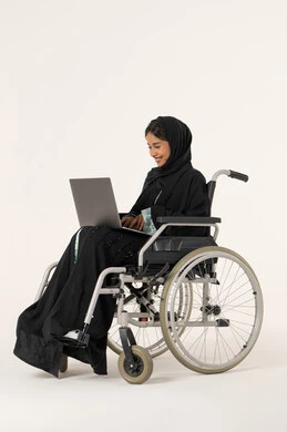 Supervising remote work, completing tasks via laptop, using modern devices and technologies, economics and financial matters, a side portrait of an Emirati Arab woman with special needs wearing an abaya and hijab sitting in a wheelchair working on a laptop, white background. Supervising remote work, completing tasks via laptop, using modern devices and technologies, economics and financial matters, a side portrait of an Emirati Arab woman with special needs wearing an abaya and hijab sitting in a wheelchair working on a laptop, white background.