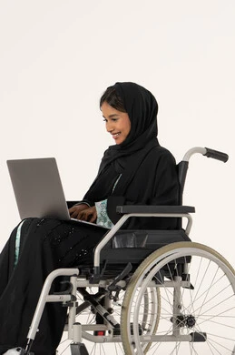 تنظيم وإدارة المهام المهنية عن بعد ,انجاز المهام عبرالابتوب , استخدام الأجهزة والتقنيات الحديثة, الاقتصاد والأمور المالية، بورترية من الجانب لامراة عربيه خليجيه اماراتية من ذوى الاحتياجات الخاصة ترتدي العباءة و الحجاب تجلس على كرسي متحرك تعمل على الحاسوب المحمول، خلفية بيضاء