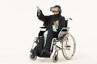 إيماءات الاندماج والتفاعل مع العالم الخيالى، الاشارة الى شيء ما، المتعة والتسلية بالمشاهدة عبر نظارة الواقع الافتراضي، بورترية لشابة عربيه خليجيه اماراتية من ذوى الاحتياجات الخاصة ترتدي العباءة و الحجاب ونظارات ثلاثية الأبعاد (الفي ار) تجلس على كرسي متحرك، التطور التقني والتكنولوجي ، خلفية بيضاء