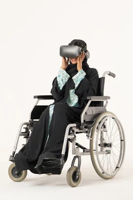 The enjoyment of entertainment viewing with virtual reality technologies, the immersion and simulation of the imaginary world, a portrait of a young Arab Gulf Emirati woman with special needs wearing an abaya and hijab and 3D glasses (VR) sitting in a wheelchair, technological and technical development, white background.