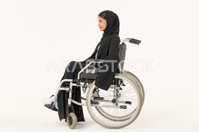 العنايه بأصحاب الهمم وتأمين احتياجاتهم الخاصة، توفير اجهزة ومعدات تساعد بالحركة والتنقل، بورتريه من الجانب لامرأة عربية اماراتية خليجية محجبة من ذوي الاحتياجات الخاصة ترتدي العباءة السوداء و تجلس على كرسي متحرك, خلفية بيضاء