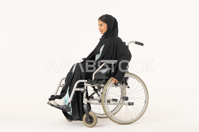 ايماءات التفاؤل بالمستقبل, تأمين أجهزة ومعدات تساعد على الحركة,  بورتريه من الجانب لامرأة عربية اماراتية خليجية محجبة من ذوي الاحتياجات الخاصة ترتدي العباءة السوداء و تجلس على كرسي متحرك, خلفية بيضاء