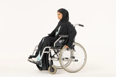 ايماءات التفاؤل بالمستقبل, تأمين أجهزة ومعدات تساعد على الحركة,  بورتريه من الجانب لامرأة عربية اماراتية خليجية محجبة من ذوي الاحتياجات الخاصة ترتدي العباءة السوداء و تجلس على كرسي متحرك, خلفية بيضاء