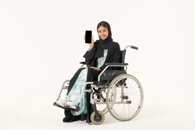 تسهيل حياة ذوي الهمم باستخدام التقنيه والتكنولوجيا, شاشة سوداء فارغه على الهاتف المحمول,  بورتريه لإمرأة عربية خليجية اماراتية خليجية محجبة مبتسمة من ذوي الاحتياجات الخاصة ترتدي العباءة السوداء و تجلس على كرسي متحرك و  تقوم بعرض برامج وتطبيقات ذوي الاحتياجات الخاصه, خلفية بيضاء