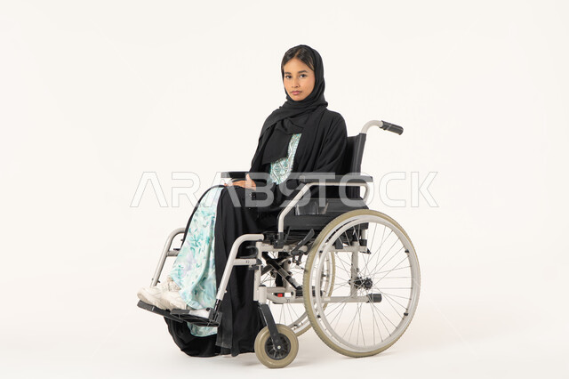 تحسين حياة ذوي الاعاقه الحركيه، ايماءات السعاده والتفاؤل بالحياه, بورتريه لإمرأة عربية عربية خليجية اماراتية خليجية محجبة من ذوي الاحتياجات الخاصة ترتدي العباءة السوداء و تجلس على كرسي متحرك و تنظر للكاميرا بثقة, خلفية بيضاء
