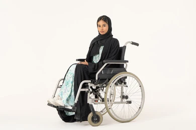 تحسين حياة ذوي الاعاقه الحركيه، ايماءات السعاده والتفاؤل بالحياه, بورتريه لإمرأة عربية عربية خليجية اماراتية خليجية محجبة من ذوي الاحتياجات الخاصة ترتدي العباءة السوداء و تجلس على كرسي متحرك و تنظر للكاميرا بثقة, خلفية بيضاء