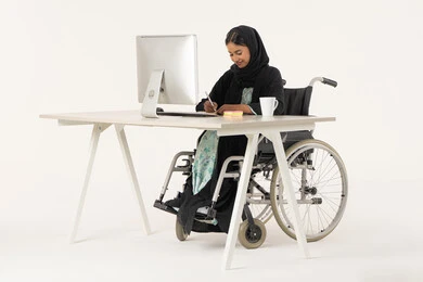 Gestures of concentration and contemplation, portrait of a veiled Emirati Gulf Arab woman with special needs wearing a black abaya and sitting in a wheelchair in front of a computer, holding a pen in her hand, taking notes on papers, preparing reports and files for work, white background Gestures of concentration and contemplation, portrait of a veiled Emirati Gulf Arab woman with special needs wearing a black abaya and sitting in a wheelchair in front of a computer, holding a pen in her hand, taking notes on papers, preparing reports and files for work, white background