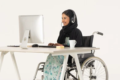 To answer customers' questions, a portrait of a veiled Emirati Gulf Arab woman with special needs wearing a black abaya, sitting in a wheelchair in front of a computer and wearing headphones, office administrative professions and jobs, business affairs management and organization, white background