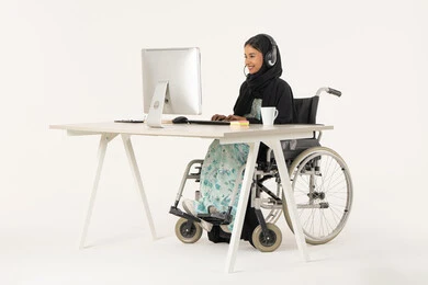 مفهوم الاستعلامات والاستفسارات، العمل في مجال خدمة العملاء، بورتريه لامرأة عربية اماراتية خليجية محجبة من ذوي الاحتياجات الخاصة ترتدي العباءة السوداء و تجلس على كرسي متحرك أمام جهاز الكمبيوتر و تضع سماعات الهيدفون, مهن ووظائف ادارية مكتبية، خلفية بيضاء