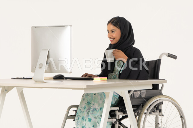 الحيوية والنشاط عند شرب الكافيين، مهن ووظائف ادارية مكتبية, إدارة شؤون الأعمال وتنظيمها، بورتريه لامرأة عربية اماراتية خليجية محجبة من ذوي الاحتياجات الخاصة ترتدي العباءة السوداء و تجلس على كرسي متحرك و تباشر عملها من خلال الكمبيوتر و تشرب مشروب دافئ, خلفية بيضاء