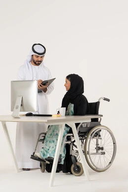 Journaling and writing on paper, discussing work between colleagues, office administrative professions and jobs, portrait of a veiled Arab Emirati Gulf woman with special needs wearing a black abaya and sitting in a wheelchair, discussing with her Emirati colleague who is wearing a white kandura and ghutra and holding a paper holder, white background
