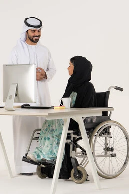 أهمية النقاش و الحوار في العمل, مهن ووظائف ادارية مكتبية, بورتريه لامرأة عربية اماراتية خليجية محجبة من ذوي الاحتياجات الخاصة ترتدي العباءة السوداء و تجلس على كرسي متحرك و تتناقش مع زميلها الاماراتي المبتسم الذي برتدي الكندورة والغترة البيضاء, خلفية بيضاء