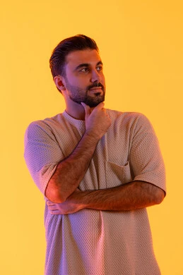 الوقوف برجولة والنظر إلى شيء ما ، مفهوم الاندماج والتركيز، بورتريه لرجل عربي خليجي اماراتي يرتدي االزي الكاجوال ينظر للكاميرا بإيماءات التفكير والتفاعل، توقع الاحداث والتنبئ بها، مفهوم الاناقة و الاهتمام بالمظهر الخارجي, خلفية برتقاليه