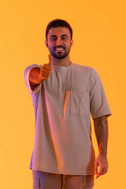 الإشارة باصبع الإبهام نحو الأعلى تعابير القبول والفرح والسرور، مفهوم الاتفاق والموافقه، التعبير عن الجودة الممتازة، بورتريه لرجل عربي خليجي اماراتي يرتدي االزي الكاجوال ينظر للكاميرا بإيماءات الرضا، مفهوم الاناقة و الاهتمام بالمظهر الخارجي, خلفية برتقاليه