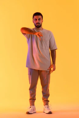 الإشارة باصبع الإبهام نحو الأسفل بعلامات السوء وعدم القبول، الشعور بالانزعاج والاضطراب, التعبير عن الجودة السيئة، بورتريه لرجل عربي خليجي اماراتي يرتدي االزي الكاجوال ينظر للكاميرا بإيماءات الغضب، مفهوم الاناقة و الاهتمام بالمظهر الخارجي, خلفية برتقاليه