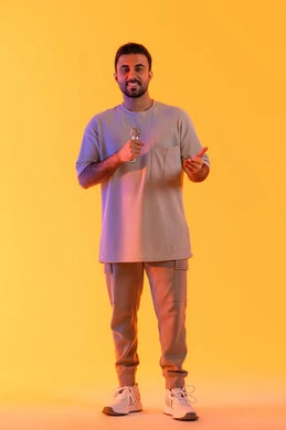 إجراء المقابلات وطرح الأسئلة، غناء مقطع صوتي غنائي، بورتريه لرجل عربي خليجي إماراتي يرتدي الزي الكاجوال يمسك المايكروفون ويغني بحماس، إيماءات الإندماج والتفاعل، التواصل الفعال وتبادل الحوارات، الجسم بالطول الكامل، خلفية برتقالي .