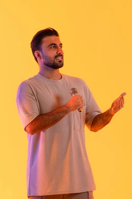 Entertainment segments and theatrical performances, singing a vocal music clip, a portrait of an Arab Gulf Emirati man wearing casual attire holding a microphone and singing enthusiastically, gestures of engagement and interaction, conducting interviews and asking questions, effective communication and exchanging dialogues, orange background.