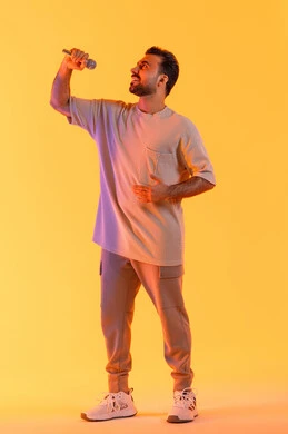 تقديم العروض الفنية المسرحية والفقرات الترفيهية، غناء مقطع صوتي غنائي، بورتريه لرجل عربي خليجي إماراتي يرتدي الزي الكاجوال يمسك المايكروفون ويغني بحماس، إيماءات الإندماج والتفاعل، إجراء المقابلات وطرح الأسئلة، التواصل الفعال وتبادل الحوارات، خلفية برتقالي .