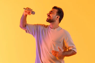 تسجيل مقطع صوتي غنائي، بورتريه لرجل عربي خليجي إماراتي يرتدي الزي الكاجوال يمسك المايكروفون ويغني بحماس، إيماءات الإندماج والتفاعل، تقديم العروض الفنية المسرحية والفقرات الترفيهية، إجراء المقابلات وطرح الأسئلة، التواصل الفعال وتبادل الحوارات، خلفية برتقالي .